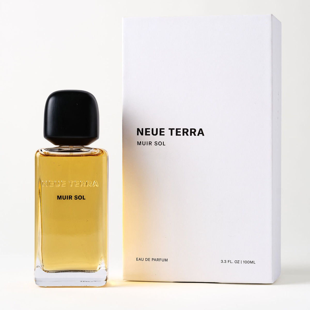 A bottle of Neue Terra Muir Sol Eau de Parfum with amber liquid and a black cap, standing next to its white packaging box on a clean white background.